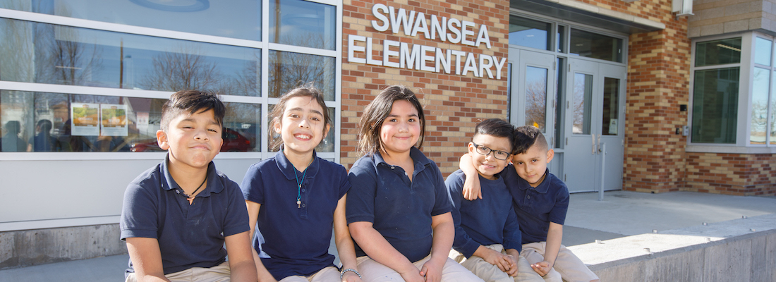 Group of students posing outside in front of school